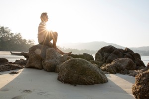 Man sits on beach boulder, looks out to view across sea thinking, "Sell my house fast to the Aida Group."