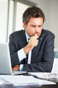 Business man in deep thought with laptop thinking sell my house fast to The Aida Group.