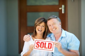 Happy mature couple holding sold sign in front of a new house
